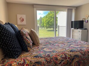 Una camera da letto con un letto grande, una televisione e vista su un prato verde attraverso una porta scorrevole.