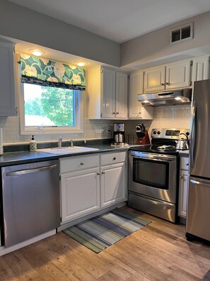 Una cocina moderna con armarios blancos, electrodomésticos de acero inoxidable, un ventanal con un adornado de flores y una alfombra estampada.
