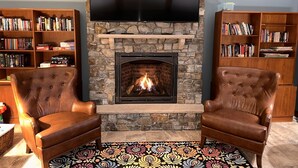 Una sala de estar acogedora con una chimenea de piedra, dos sillones de cuero y estanterías llenas de libros.