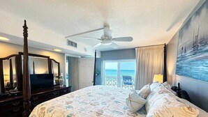 A spacious bedroom with a large bed, a ceiling fan, a TV, and a view of the ocean through the window. - El Matador 362 -  FREE TICKETS!! Your stay includes free tickets to many area attractions! (Fort Walton Beach)