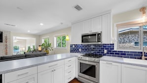 A modern kitchen with white cabinets, a stainless steel stove, and a blue-tiled backsplash. - Million-dollar View & Affordable Too! Kayaks free for use (Kingsland)