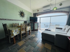 Enjoy a comfortable stay in this well-appointed living room with a large TV, dining area, and sofa overlooking the sea.