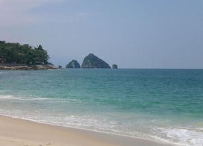 Une plage bordée d’une eau turquoise et transparente, avec des formations rocheuses visibles au loin.