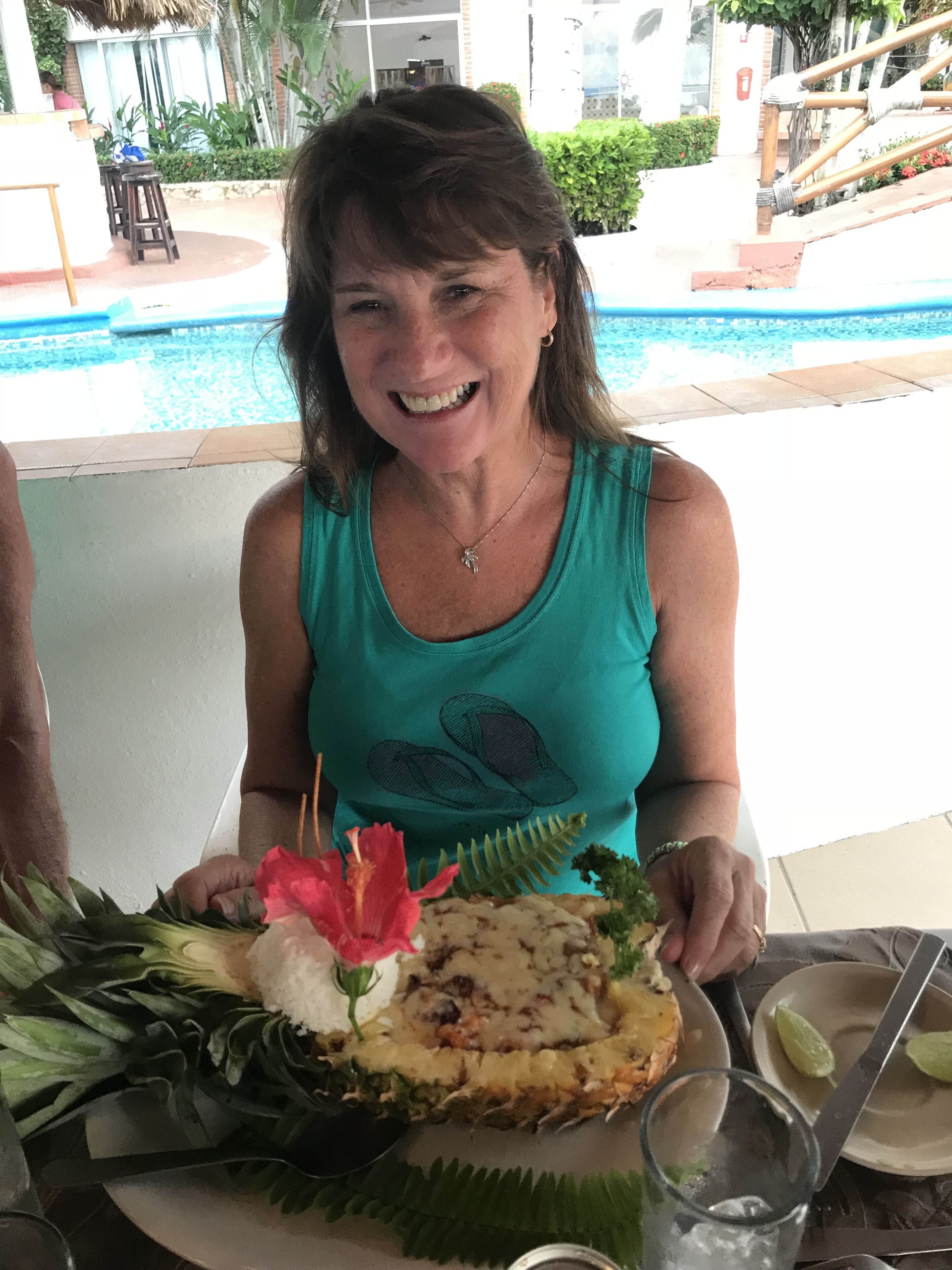 Uma pessoa sentada à mesa com um prato de comida, um copo de água e uma piscina ao fundo.