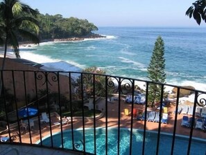 Enjoy the ocean view from this balcony, featuring a pool area with lounge chairs and umbrellas below.