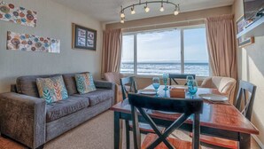 Een kamer met een bank, eettafel, stoelen, een televisie en een raam met uitzicht op de oceaan.