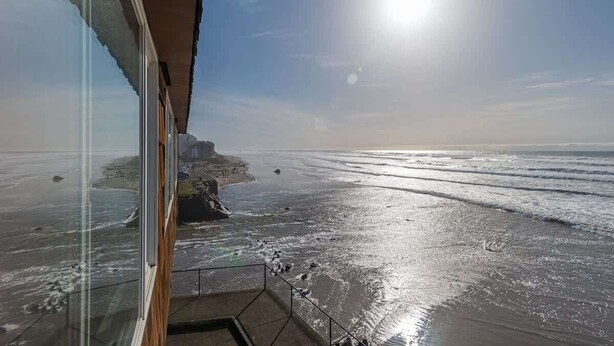 Een uitzicht op de kust vanaf een balkon, met heldere lucht en zon.