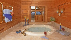 Ein Holzblockhaus-Interieur mit einer großen Badewanne, Kerzen und einer Weinflasche.