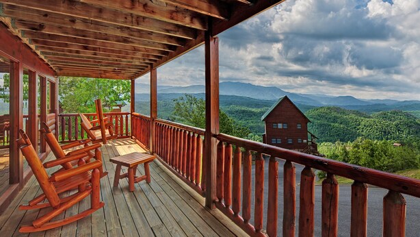 Eine Holzterrasse mit Schaukelstühlen und einem Tisch, mit Blick auf eine gebirgige Landschaft.