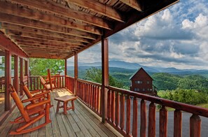 Een houten terras met schommelstoelen en een tafel, met uitzicht op een bergachtig landschap.