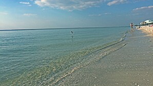 Een strand met helder water, een zandstrand en enkele mensen.
