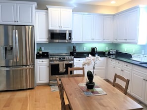 Enjoy cooking in this well-equipped kitchen with stainless steel appliances, white cabinetry, and a dining table.