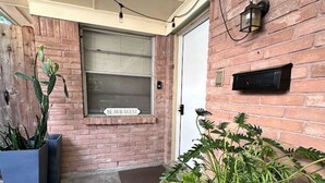 A brick exterior with a door, a window with a 'BE OUR GUEST' sign, and potted plants. - Shabby Chic Duplex Tx Medical Center, Rice Village (Houston)