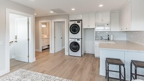 A modern kitchen with white cabinets, a double washer and dryer, a microwave, and a wooden floor.