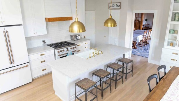 A modern kitchen with white cabinetry, a central island with stools, and a hanging brass pendant light.