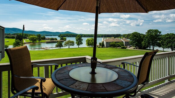 A balcony with a table and chairs, overlooking a lake and greenery. - Romantic SML Penthouse, Bernard’s Landing. Smith Mountain Lake 3 Pools (Moneta)