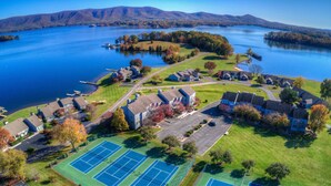 An aerial view of a lakeside residential area with houses, a tennis court, and a dock. - Romantic SML Penthouse, Bernard’s Landing. Smith Mountain Lake 3 Pools (Moneta)