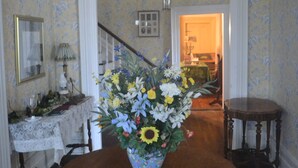 A dining room with a wooden table, a floral centerpiece, and a staircase in the background. - Historic Home - Victorian Stage Coach Inn (Russellville)
