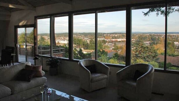 A spacious living room with large windows offering a view of a cityscape. - 'Harbor View Grand'—Grand View, Home, Hot Tub, Sauna, and Concert Grand Piano. (Oak Harbor)
