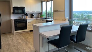 A modern kitchen with white cabinetry, a black stove, and a large window offering a view of the outdoors. - 'Harbor View Grand'—Grand View, Home, Hot Tub, Sauna, and Concert Grand Piano. (Oak Harbor)