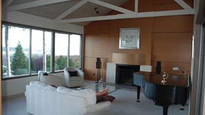 A spacious living room with a white sofa, a piano, and a fireplace. - 'Harbor View Grand'—Grand View, Home, Hot Tub, Sauna, and Concert Grand Piano. (Oak Harbor)