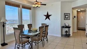 A dining area with a glass table, four chairs, a ceiling fan, and a star decoration on the wall.