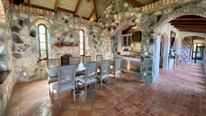 A spacious dining area with stone walls and a tiled floor, featuring a large table and chairs.