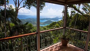A covered balcony with a view of a mountainous landscape and a body of water.