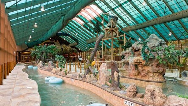 Ein Indoor-Wasserpark mit Glasdach, künstlichen Felsformationen und aufblasbaren Röhren.