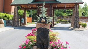 Ein Holzschild mit einem Bären, der ein 'WELCOME HOME'-Schild vor dem Eingang einer Lodge hält.