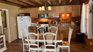 A rustic kitchen with wooden cabinets, a dining table with chairs, a refrigerator, a microwave, and hanging lights. - Weekend hiking trips at Fall Creek Falls & surrounding State Parks. (Spencer)