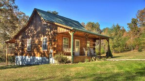 A wooden cabin with a porch and a covered front porch area, surrounded by a grassy yard and trees. - Weekend hiking trips at Fall Creek Falls & surrounding State Parks. (Spencer)