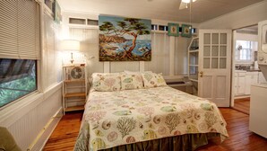 A bedroom with a bed, a ceiling fan, a painting, and a window with blinds. - Oceanfront Vintage, 1960s Cottage! Very Cozy w/Large Backyard, Ample Space, & Prime Location! (Isle of Palms)