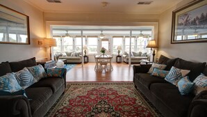 A spacious living room with two dark sofas, a red patterned rug, and a dining area with a table and chairs. - Oceanfront Vintage, 1960s Cottage! Very Cozy w/Large Backyard, Ample Space, & Prime Location! (Isle of Palms)