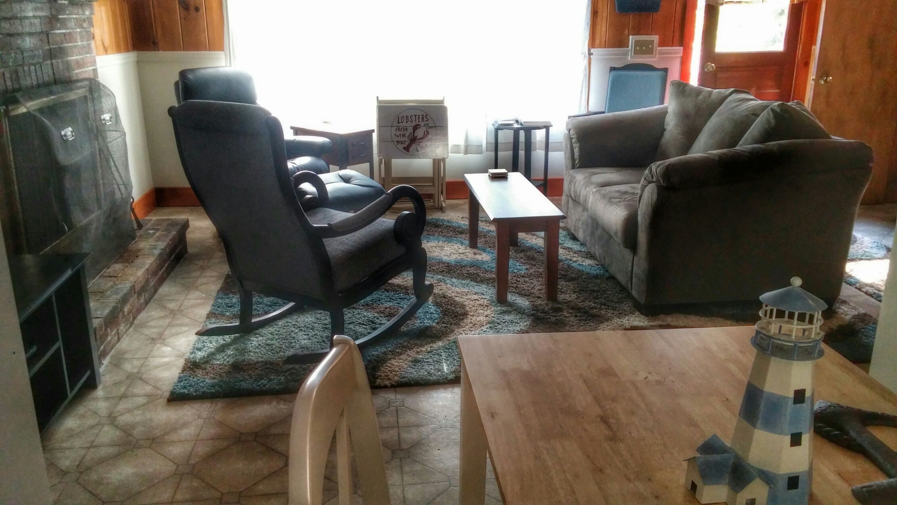 A living room with a fireplace, a sofa, a rocking chair, a small table, and a decorative lighthouse model.