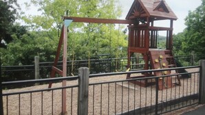 A wooden play structure with a slide and climbing area, surrounded by a fence and trees. - Modern 2000 sqft Condo with a Million Dollar Unobstructed Full Main Channel View (Lake Ozark)