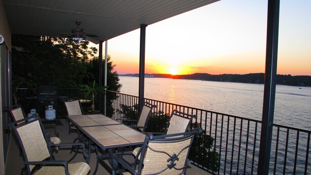 A covered outdoor seating area with a view of a sunset over a body of water. - Modern 2000 sqft Condo with a Million Dollar Unobstructed Full Main Channel View (Lake Ozark)