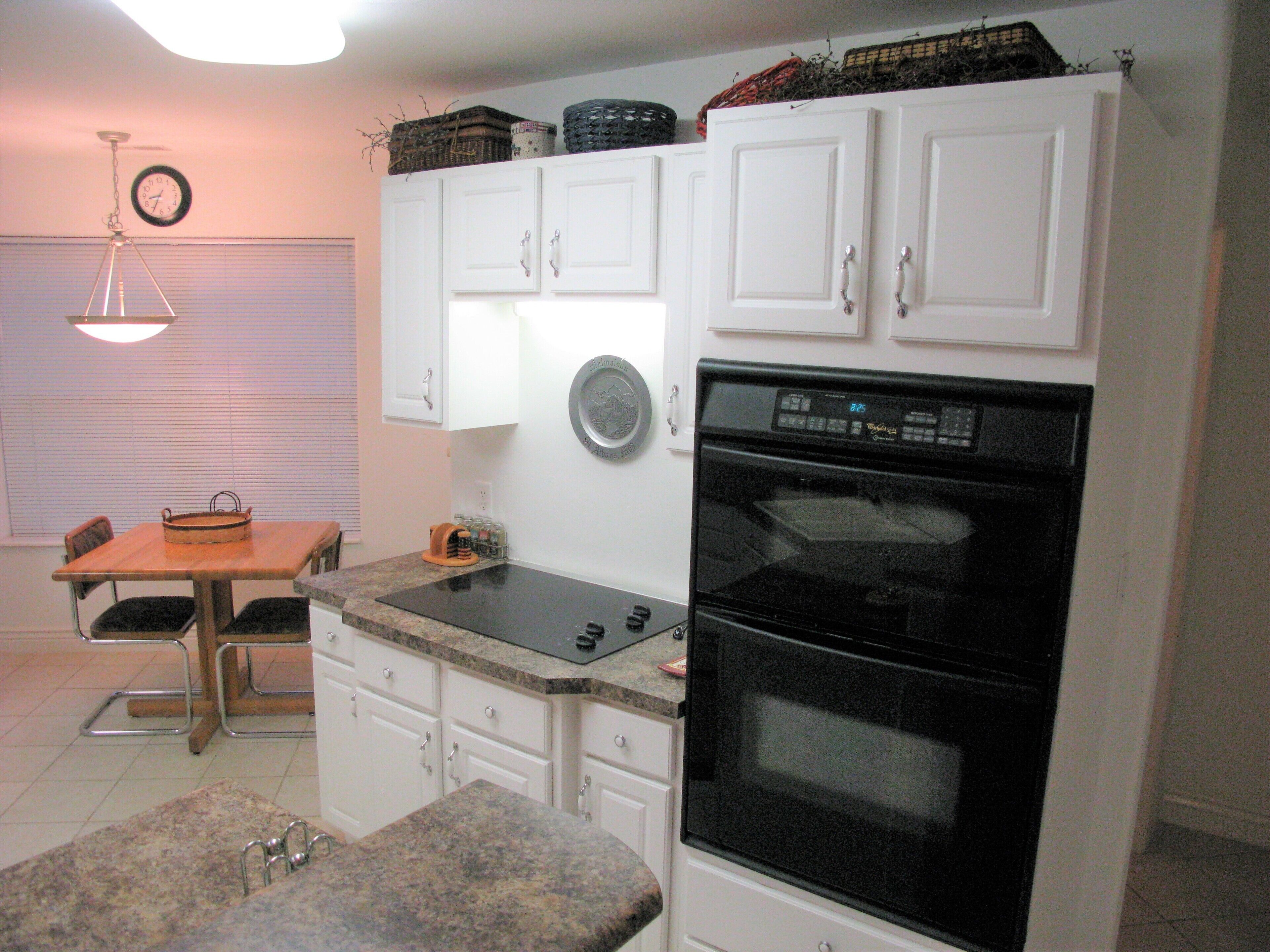 A compact kitchen with white cabinets, a black oven, and a dining area with a table and chairs.