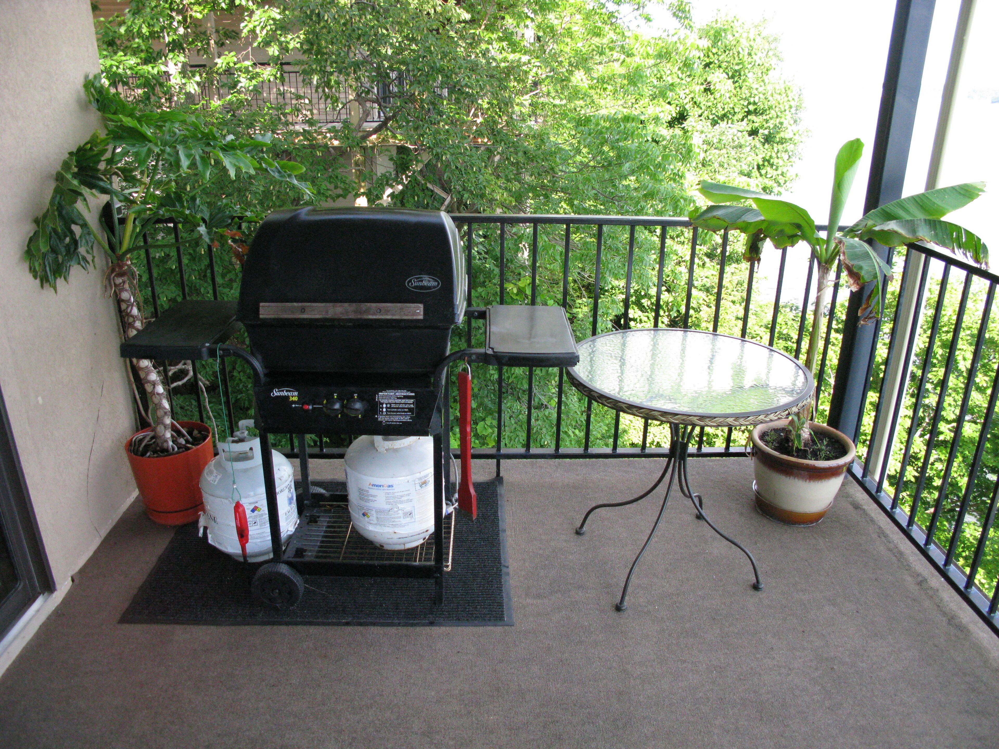 A balcony with a barbecue grill, a table, and potted plants.