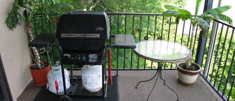 A balcony with a barbecue grill, a table, and potted plants.