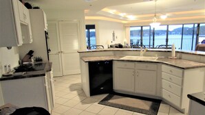A modern kitchen with white cabinets, a large island with a sink, and a view of a lake through the windows. - Modern 2000 sqft Condo with a Million Dollar Unobstructed Full Main Channel View (Lake Ozark)