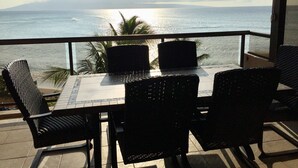 Balcón con mesa y sillas con vista a una masa de agua y una montaña distante.