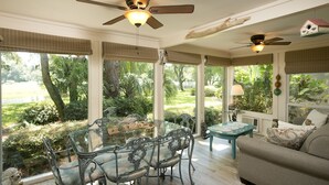 A spacious room with a glass dining table, metal chairs, a sofa, and a ceiling fan. - SeaPines, Beautifully updated, Walk to beach, Two free bikes, Pet friendly (hilton head)