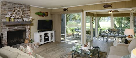 A living room with a fireplace, television, and a view of a patio with outdoor furniture.