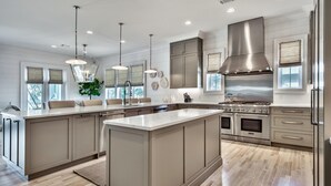 Una cocina moderna con una isla grande, electrodomésticos de acero inoxidable e iluminación colgante.
