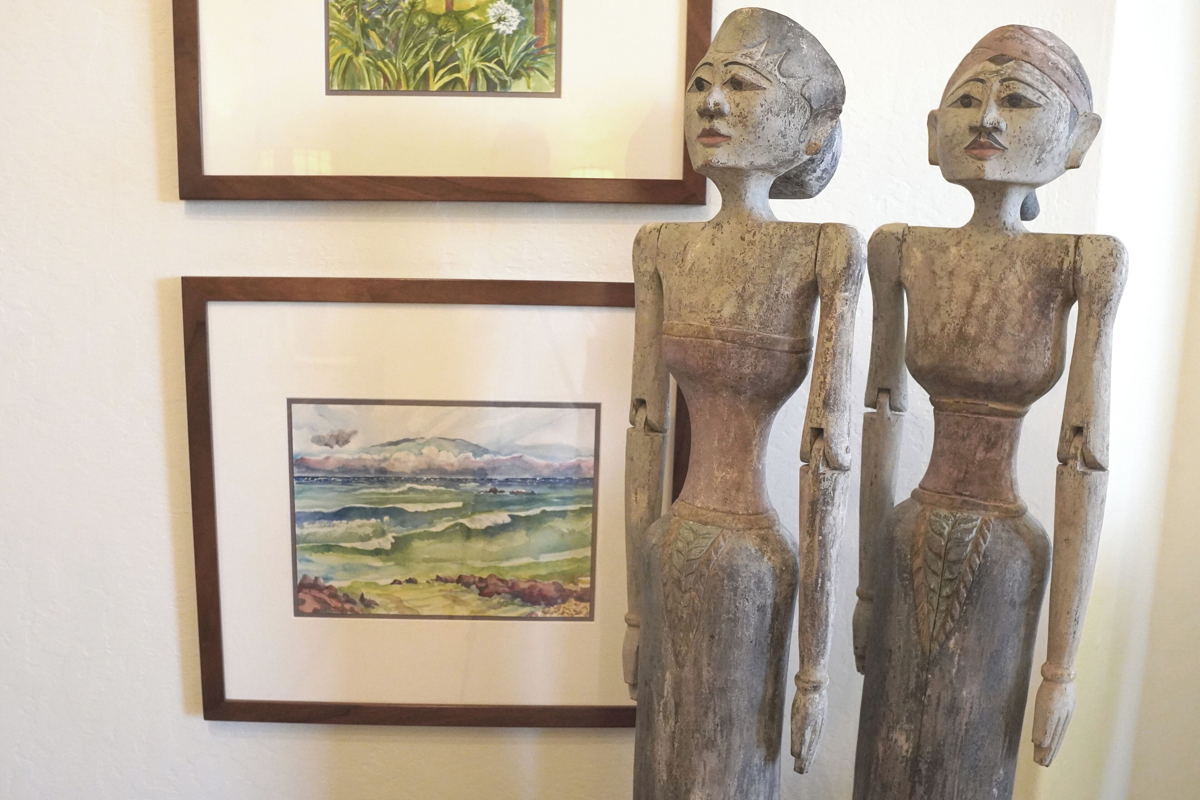 Two wooden sculptures on a wall with framed paintings above them.