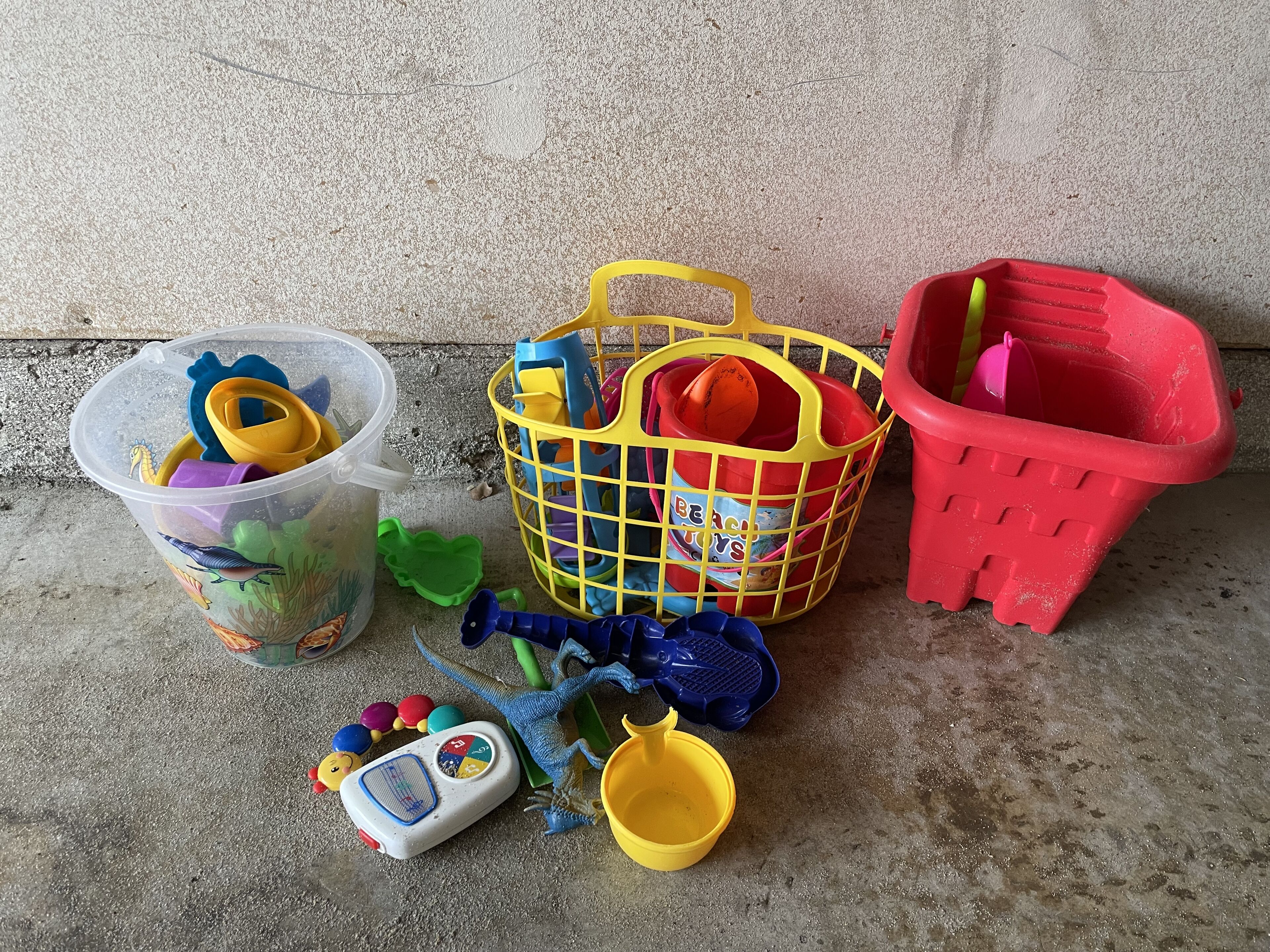 Eine Auswahl an Kinderspielzeug und Spielutensilien, darunter ein Plastikbehälter, ein gelber Korb, ein roter Plastikeimer und eine Spielwaage.