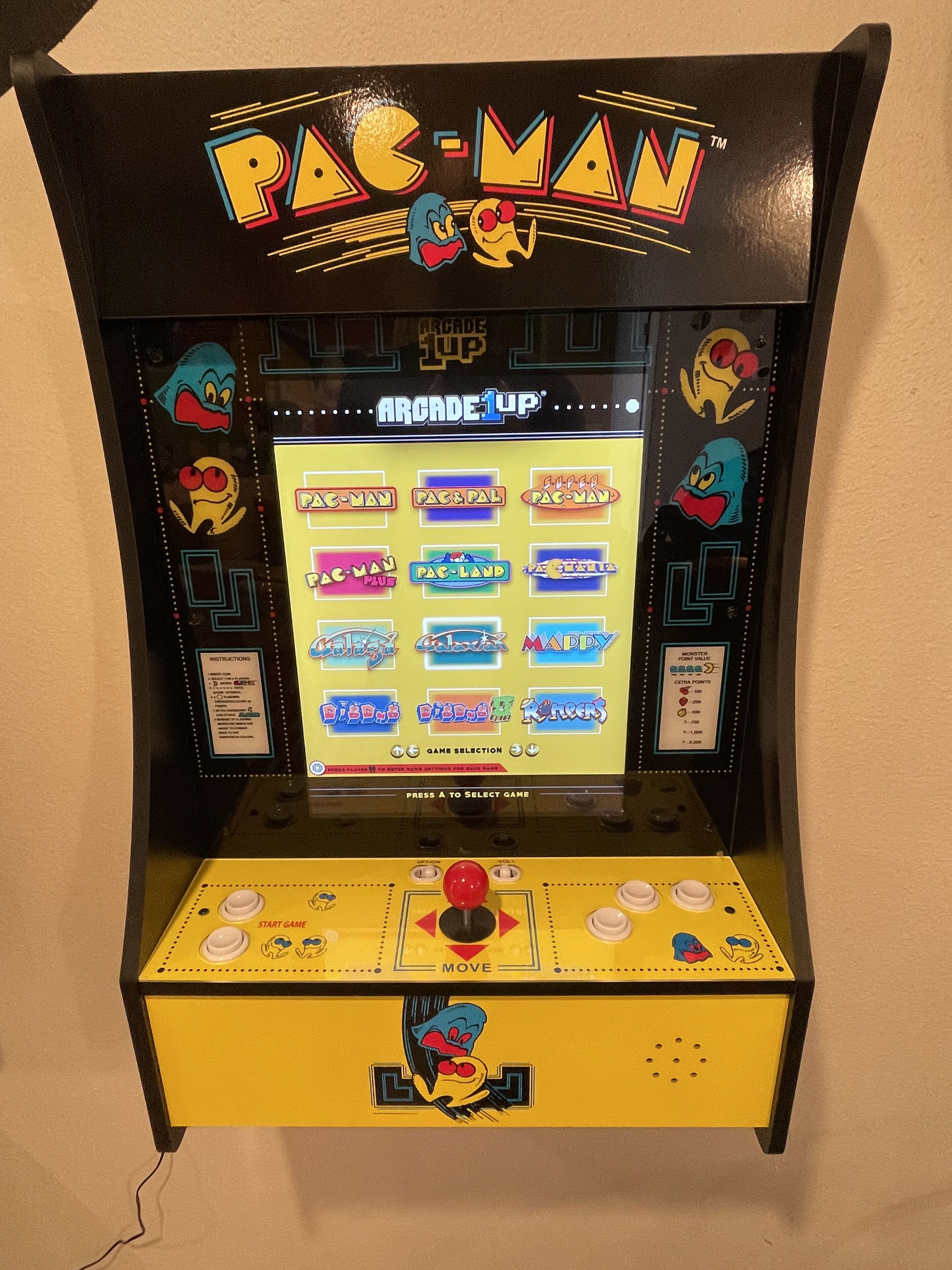 Una màquina recreativa de Pac-Man amb una base groga i una pantalla de selecció.