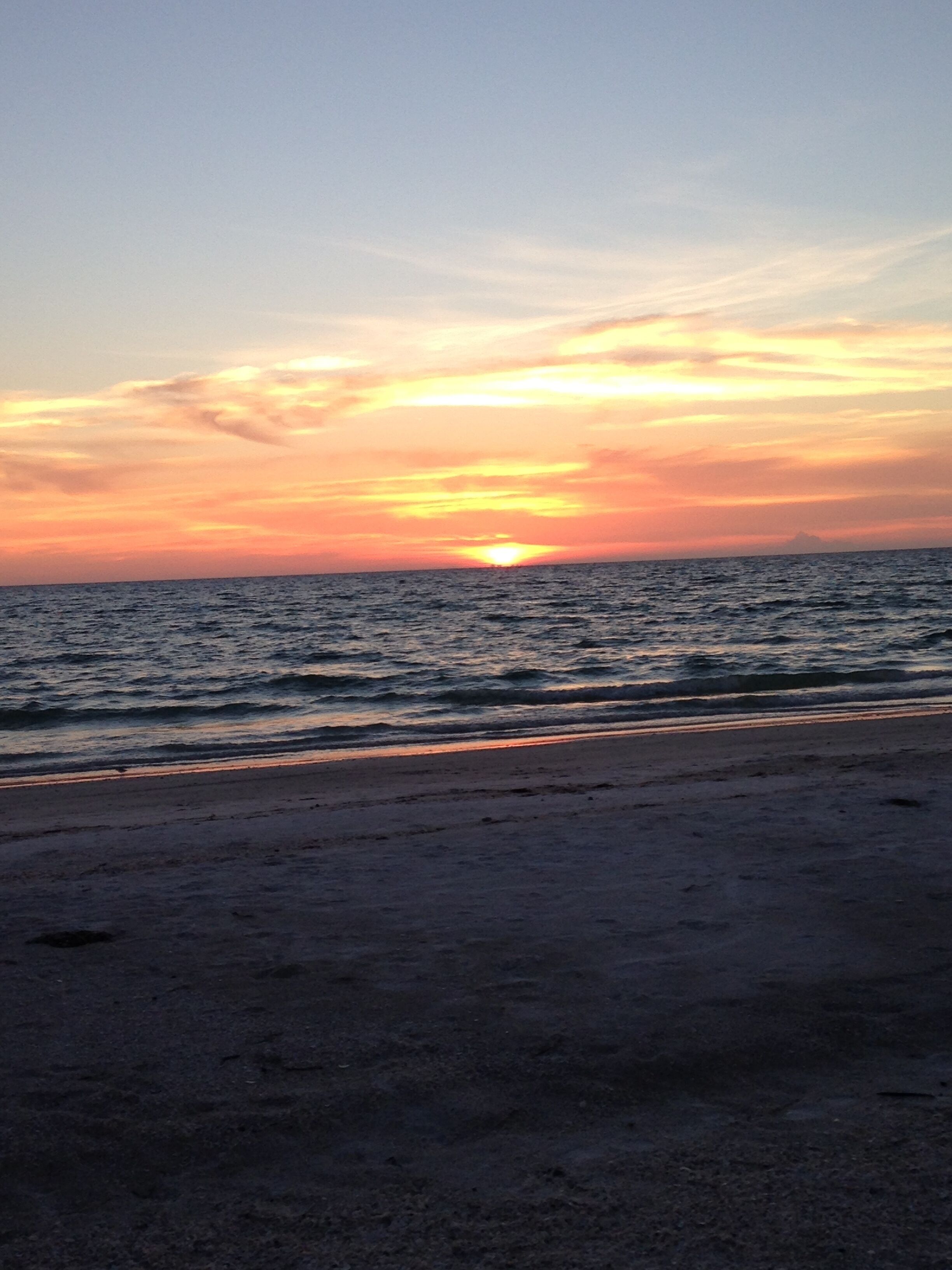 Une plage au coucher du soleil, avec l’océan et un ciel dégagé.