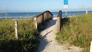 Un paseo marítimo de madera que conduce a una playa, con un letrero que indica el acceso a la playa.